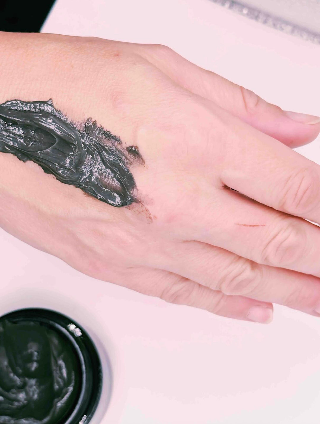 Hand with Nero Scalp And Face Mask with jar underneath with same scalp and face mask.