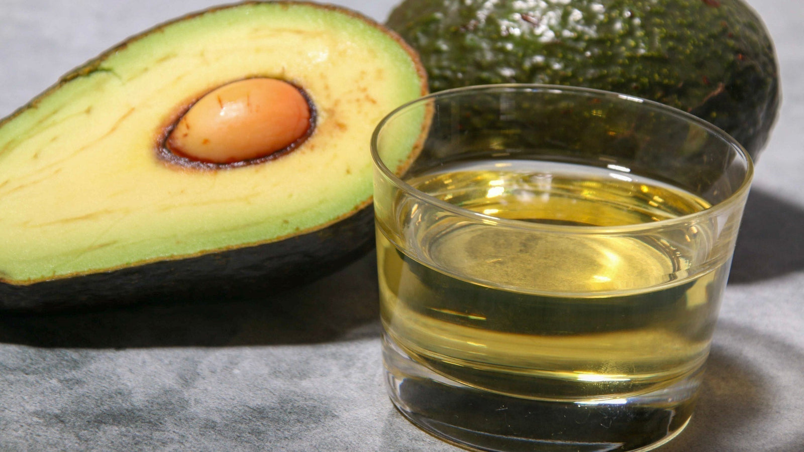 Avocado sliced in half next to avocado oil