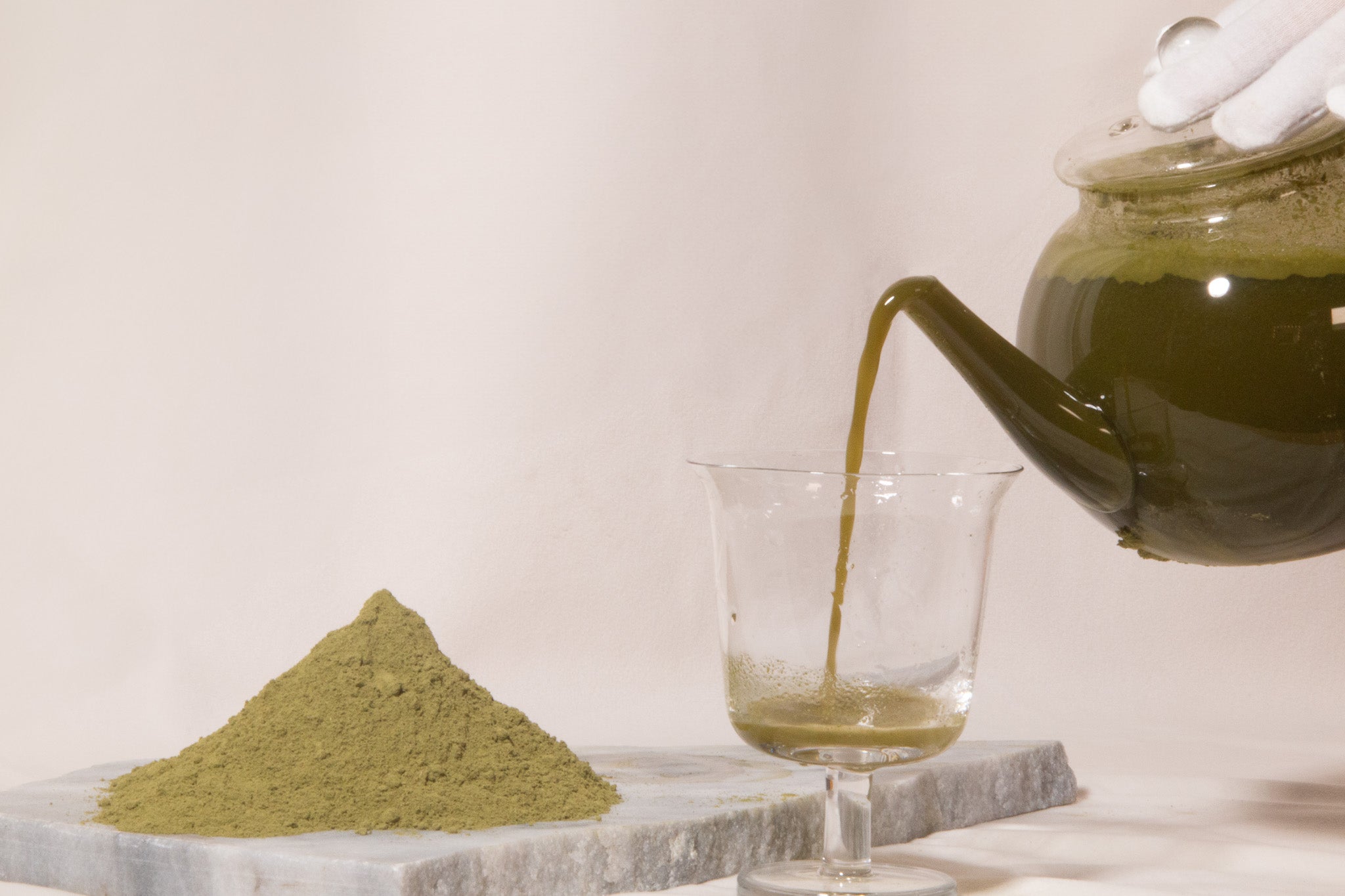 moringa powder on a marble board next to a white gloved hand pouring a glass of hot moringa tea for hair benefits