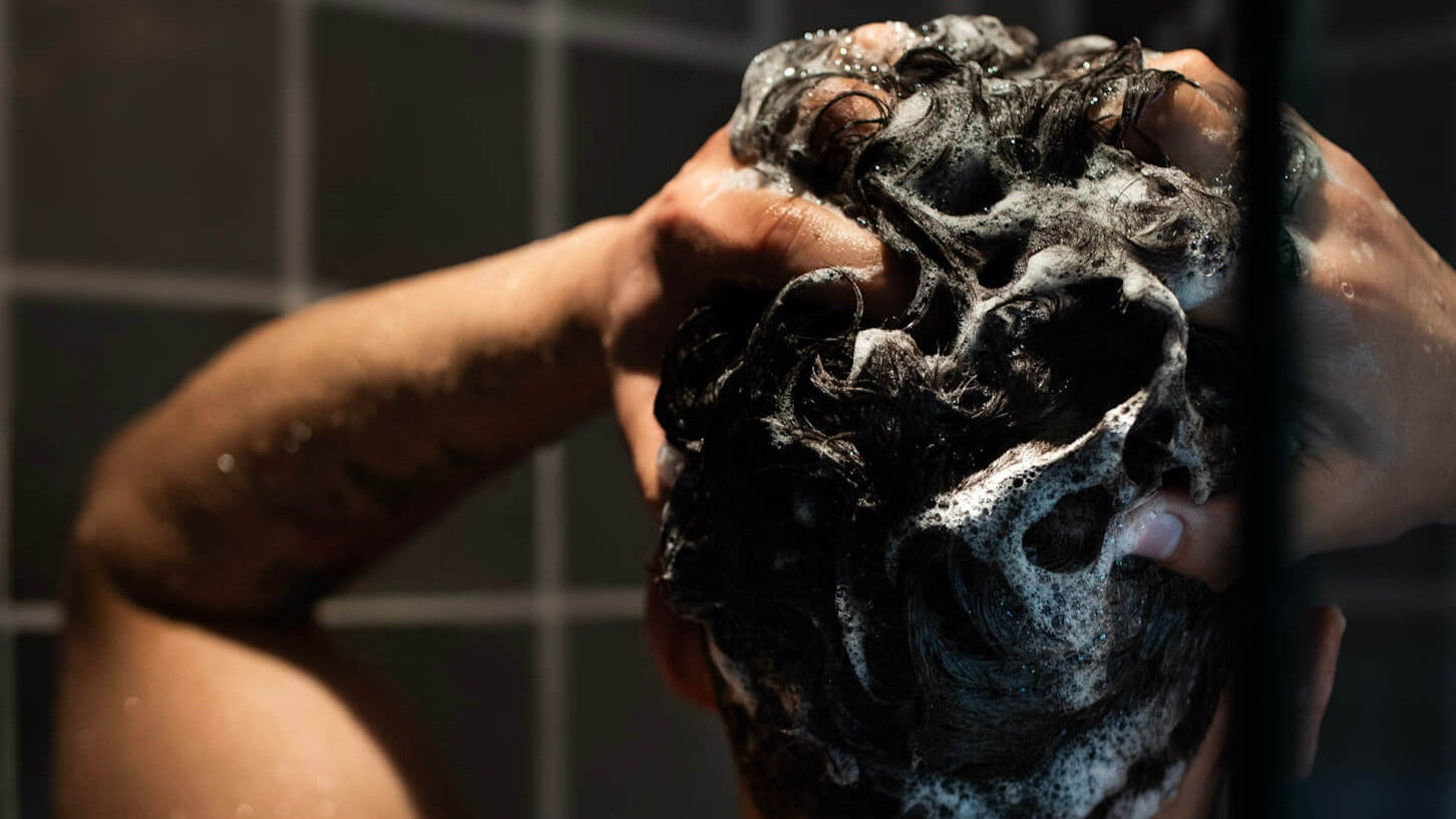 Male washing thick hair in shower 