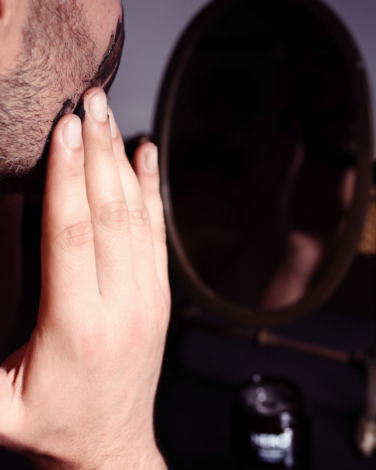 Man applying NERO Detoxifying Face and Scalp Mask to skin in front of mirror — purifying charcoal and ginger formula for clear, healthy complexion and revitalized scalp.