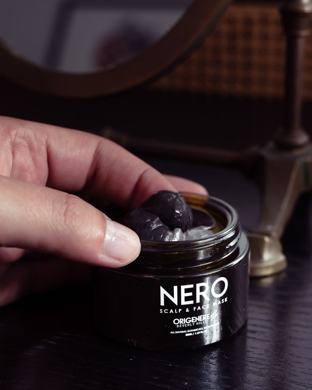 Hand scooping luxurious black detox mask from NERO Scalp and Face Mask jar by Origenere Beverly Hills — all-natural botanical skincare for deep cleansing and scalp detox.