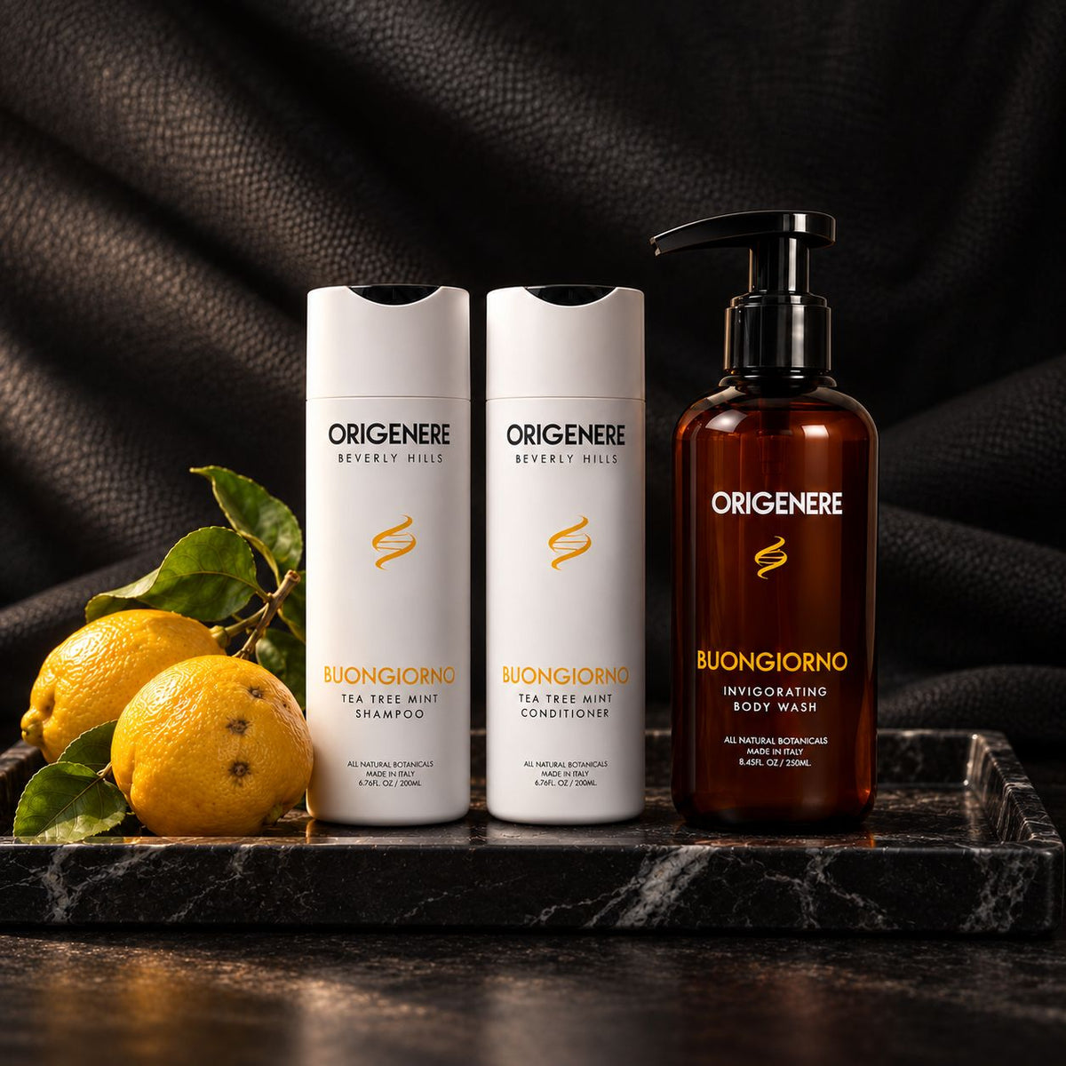 Origenere Buongiorno scalp balance collection with Tea Tree Mint Shampoo, Conditioner and Invigorating Body Wash beside fresh lemons.